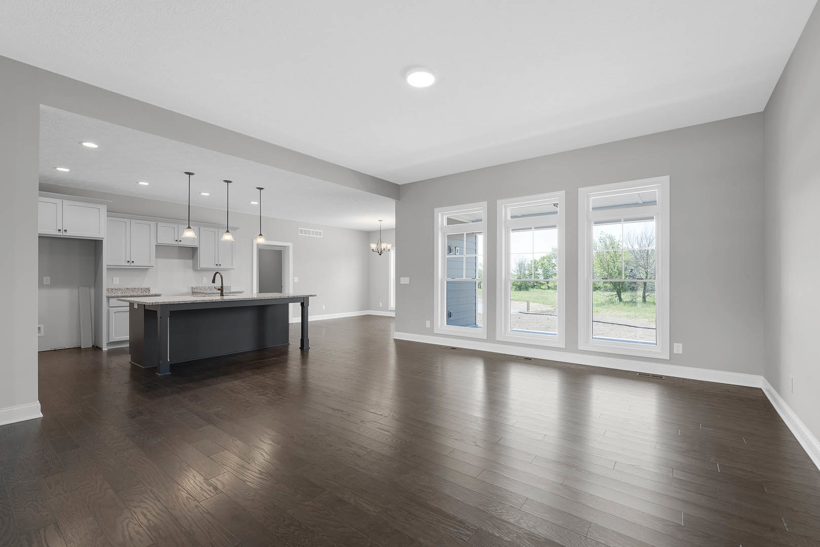 Spacious open room featuring a kitchen island with sink, hardwood floors, ceiling light fixture, plaster walls, and a row of windows overlooking trees