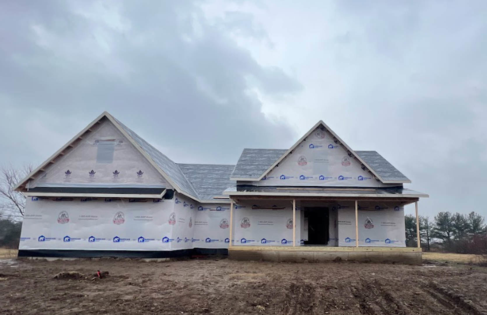 Partially built house with exposed white roofing sheets, black door framed in white, dirt field in foreground, cloudy sky overhead