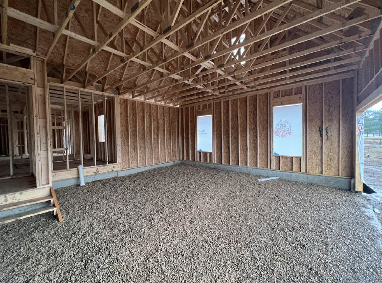 Gravel floor with wooden ladder, exposed beam ceiling, and window letting in natural light