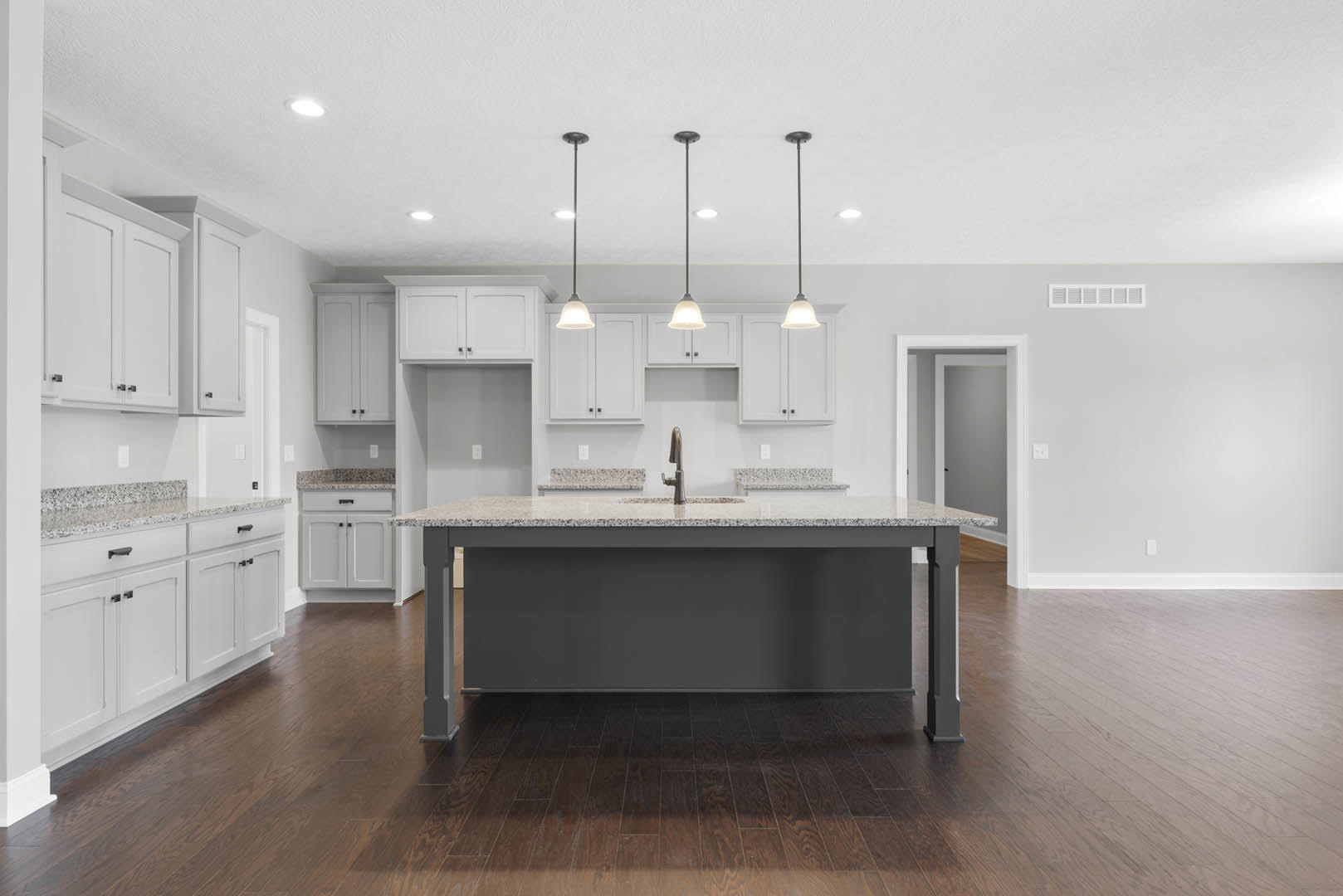 Spacious kitchen featuring a large central island with built-in sink and modern faucet, dark wood flooring, dark accent wall, overhead pendant lighting, sleek cabinetry, and