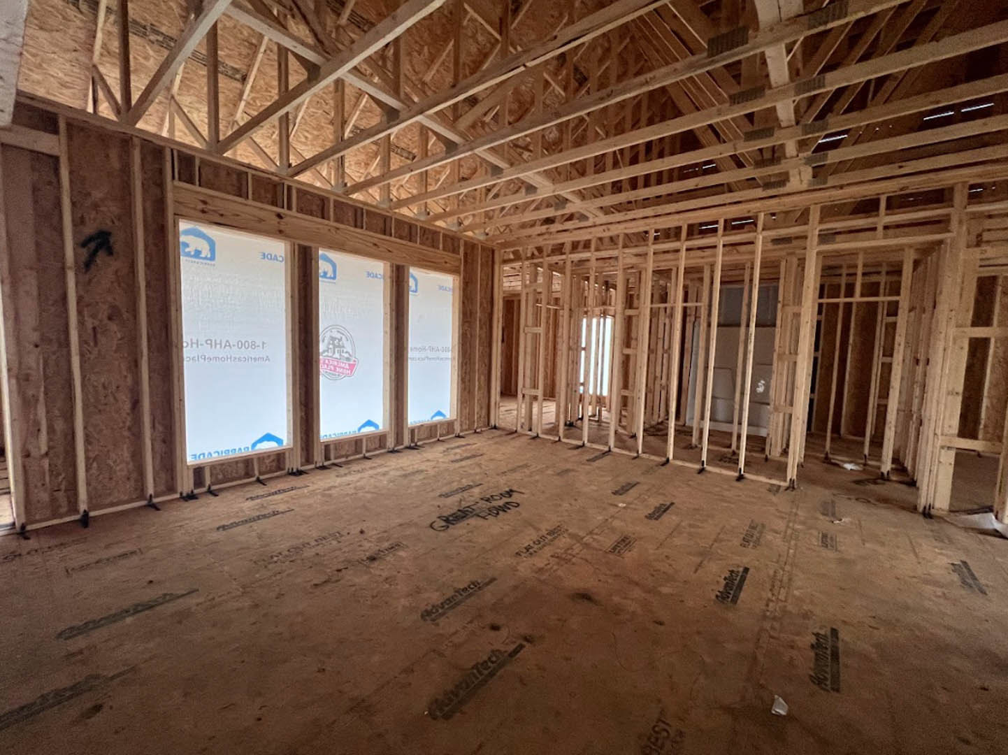 Exposed wood ceiling beams, row of large windows, unfinished floor, white sign with red and grey logo, construction materials visible in residential interior