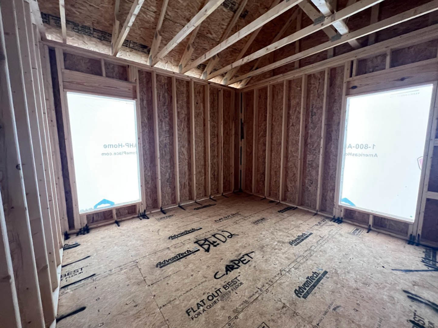 Living room with large windows, exposed wood ceiling beams, light hardwood flooring, and neutral walls.