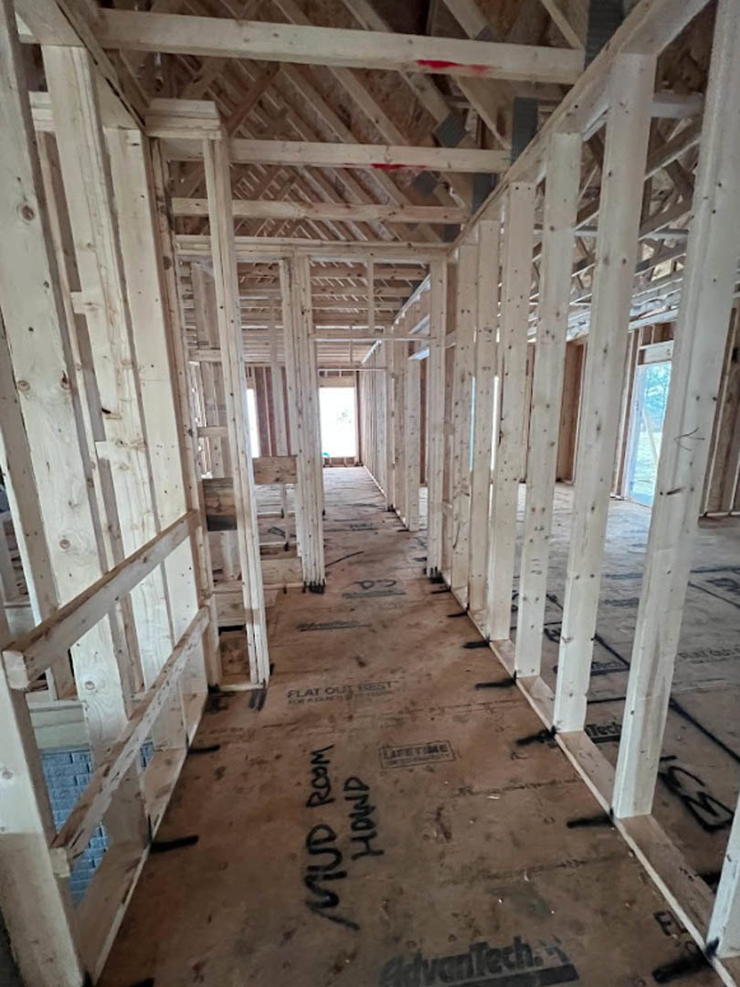 Exposed wood framing and beams inside a partially constructed house, with insulation visible between studs and daylight streaming through unfinished windows