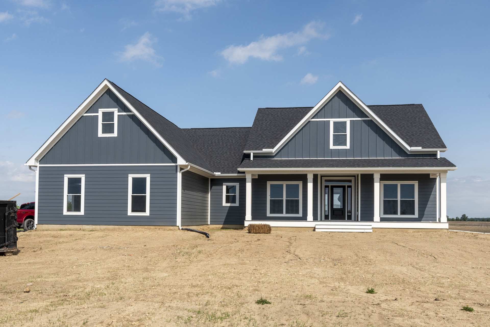 Two-story house with blue roof, white-framed windows, and large grassy yard; garden hose extends from dirt patch near foundation.