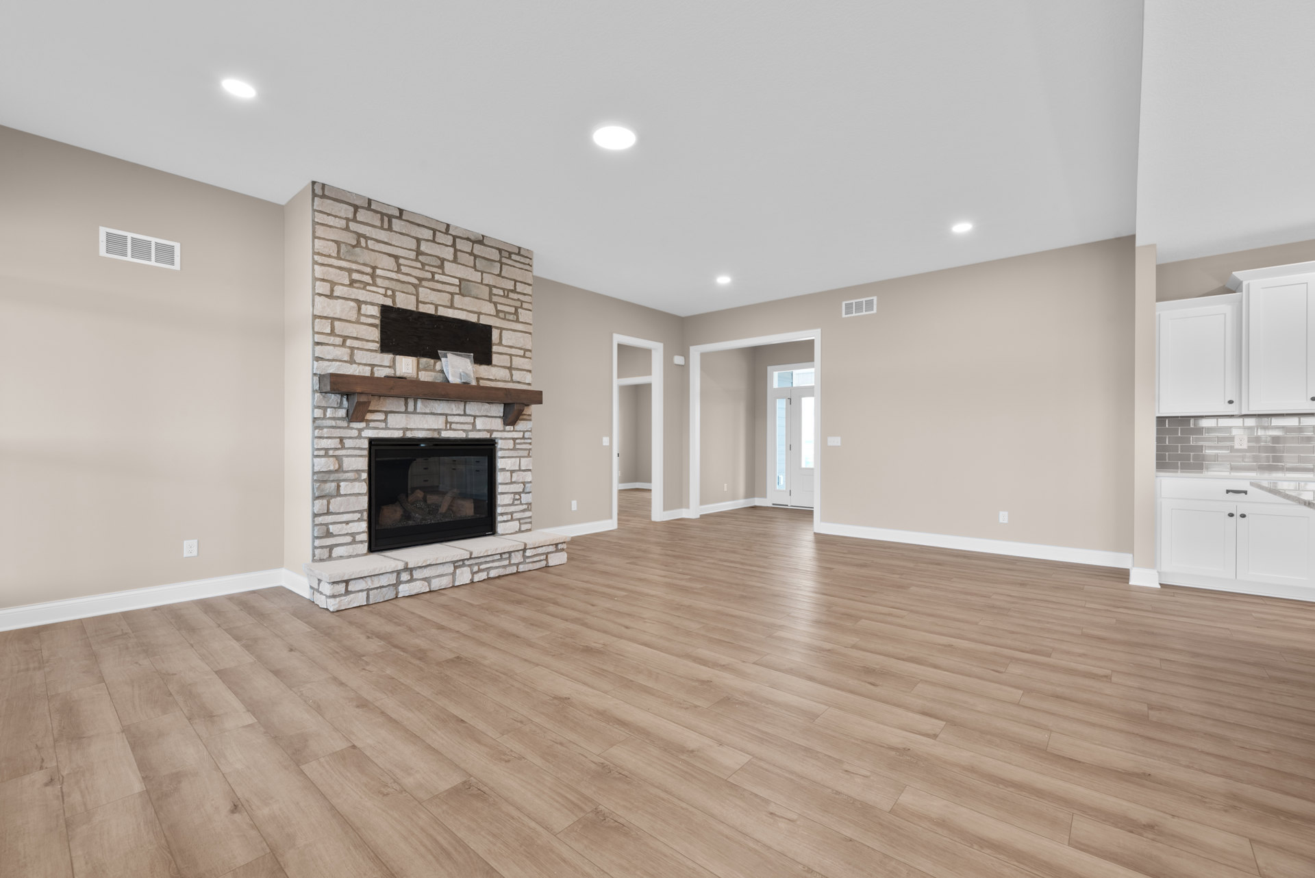 Living room featuring a central fireplace with glass doors, hardwood flooring, white ceiling light, and plaster walls; cabinetry visible along one wall.