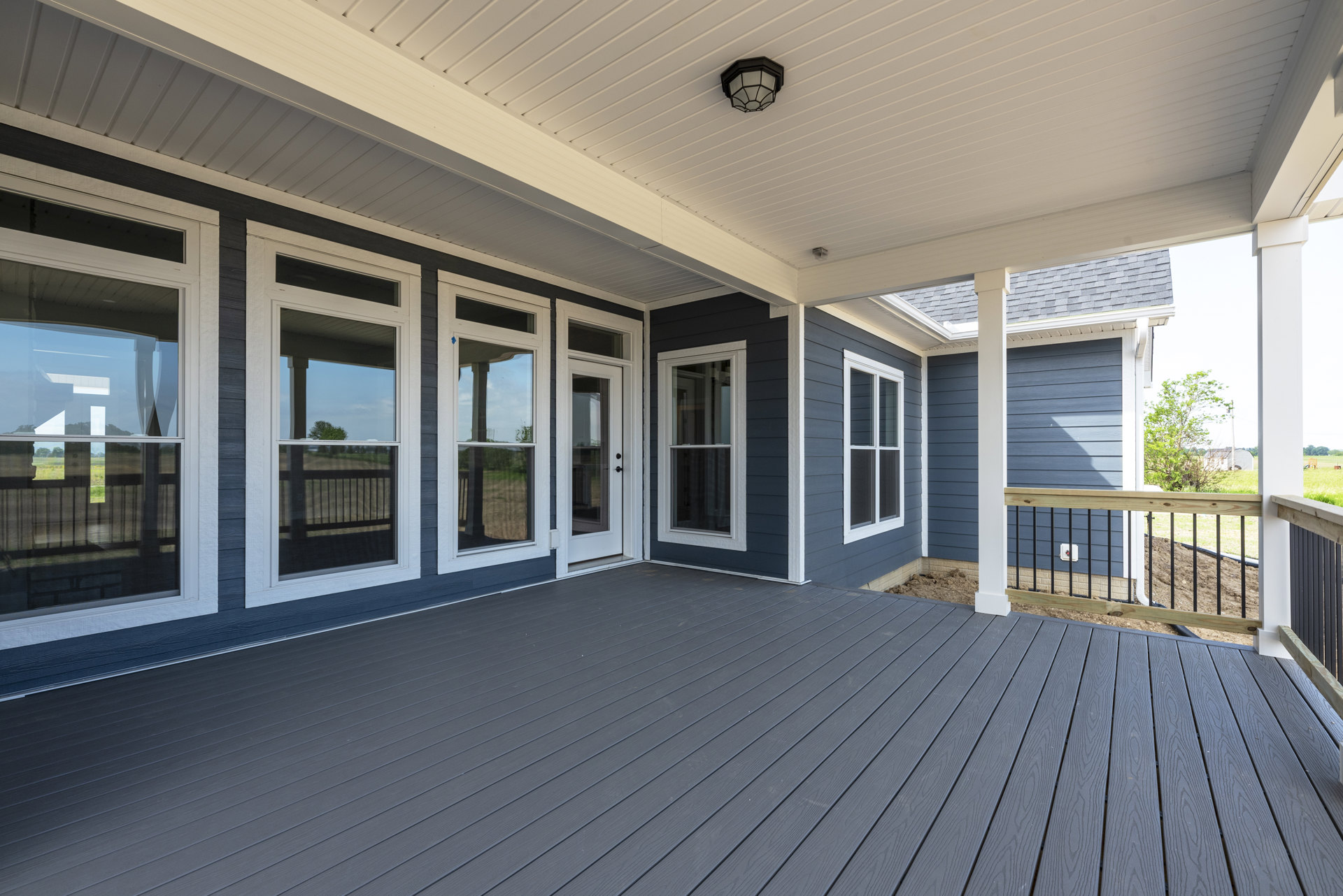 Wooden deck with white framed doors and windows, ceiling-mounted light fixture, tree visible outside window, covered porch area