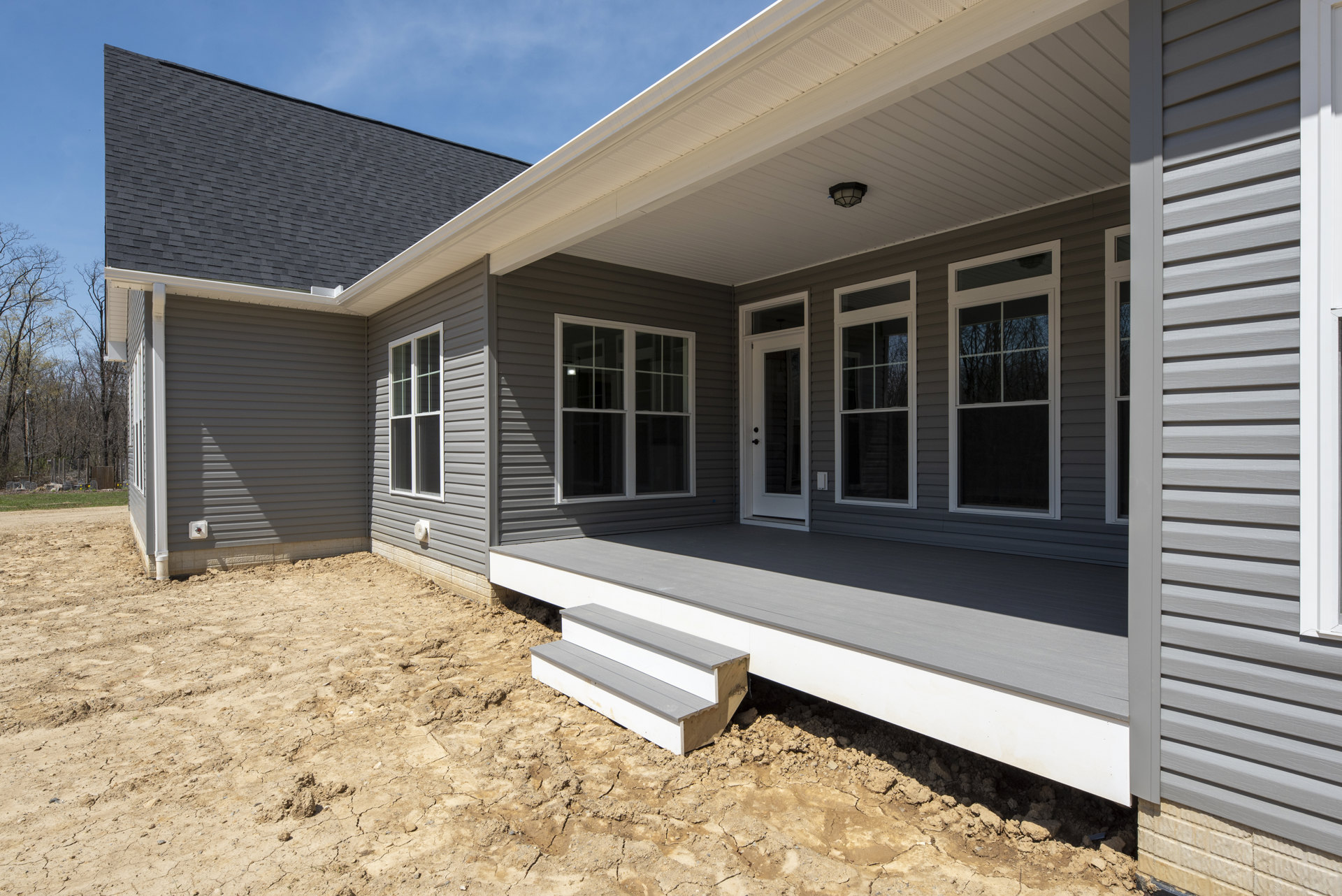 Gray siding house with white trim, covered front porch, wooden stairs, large windows reflecting trees, landscaped ground