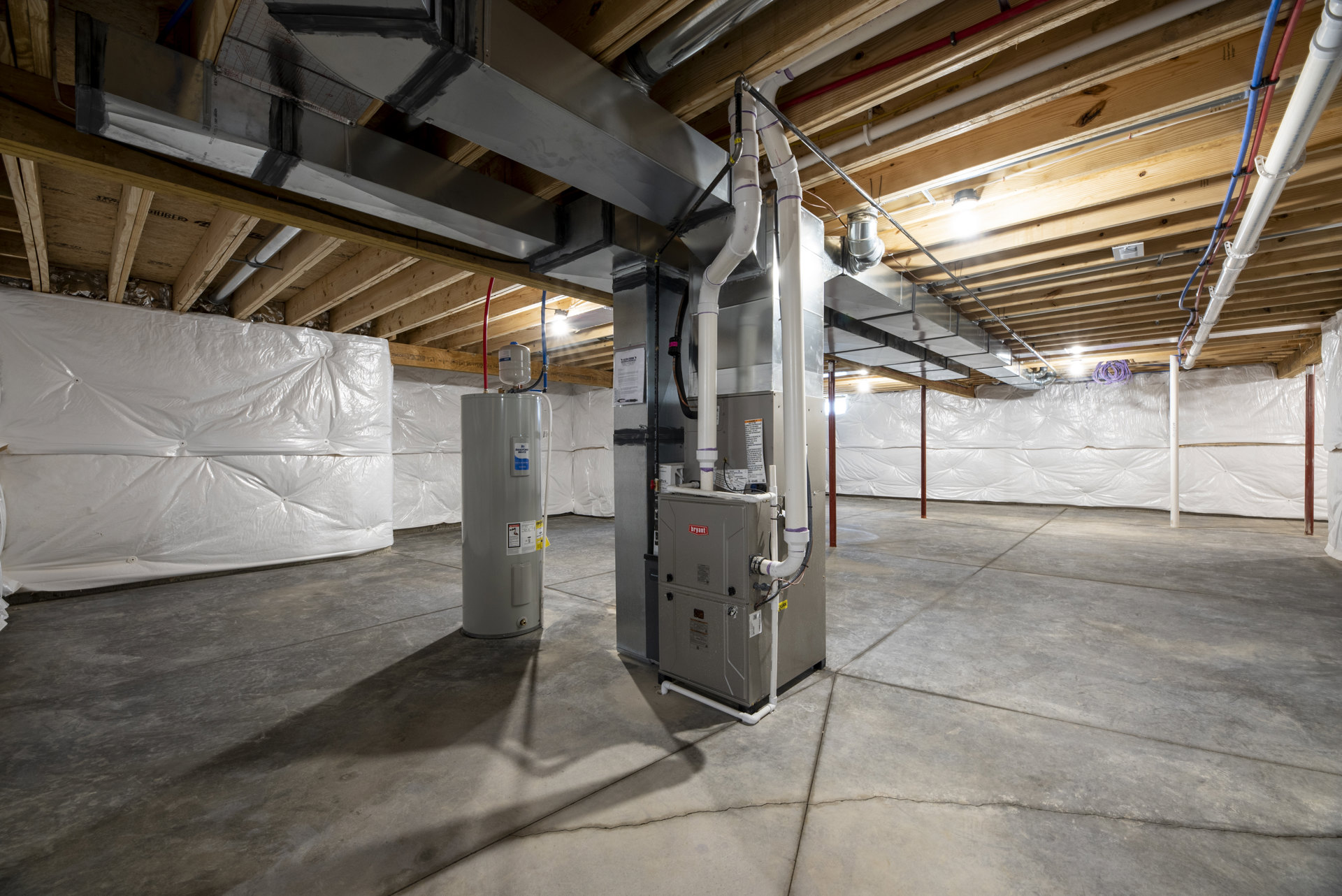 Utility room featuring a large grey metal tank with a blue label, white container with blue top, exposed metal pipes, grey rectangular control box with black buttons, and white and