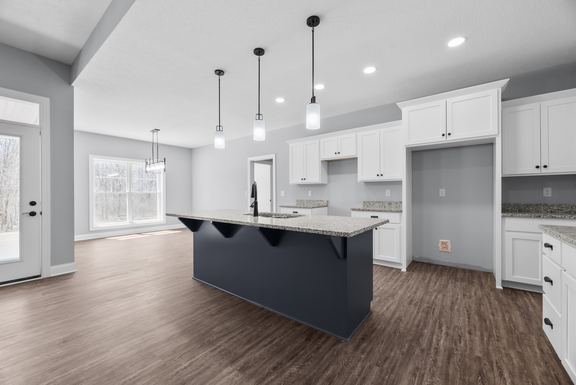 White kitchen cabinets and island with quartz countertop, stainless steel sink, pendant light fixture above, large window overlooking trees, hardwood flooring, and modern
