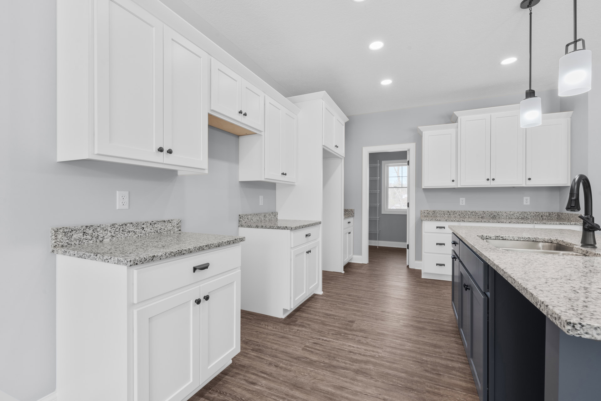 White kitchen with granite countertops, wood flooring, stainless steel faucet, and modern lighting fixtures