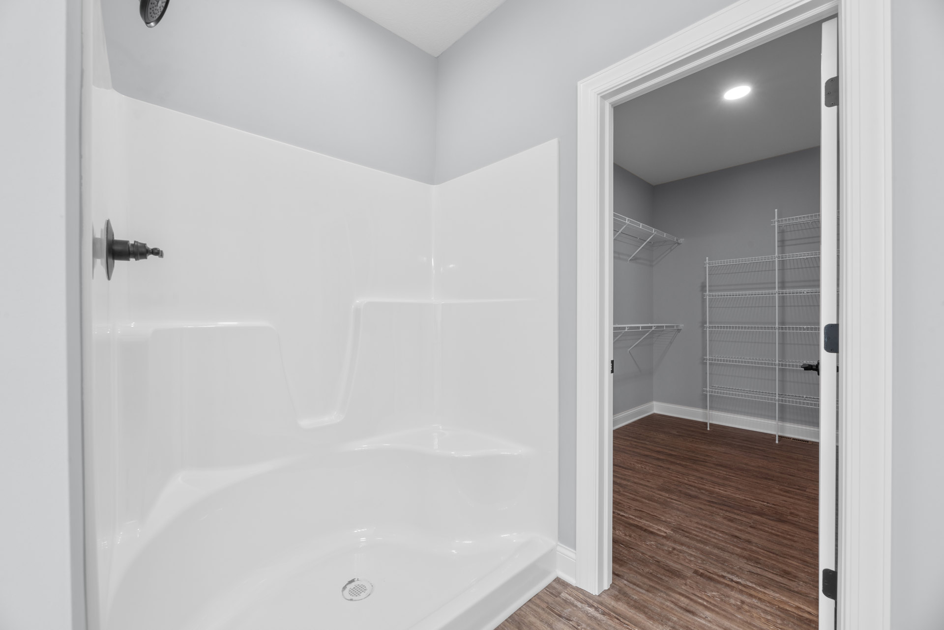 Bathroom with wood flooring, glass-enclosed shower, white bathtub with visible drain, wall-mounted white metal shelf, ceiling light fixture, and neutral tile walls