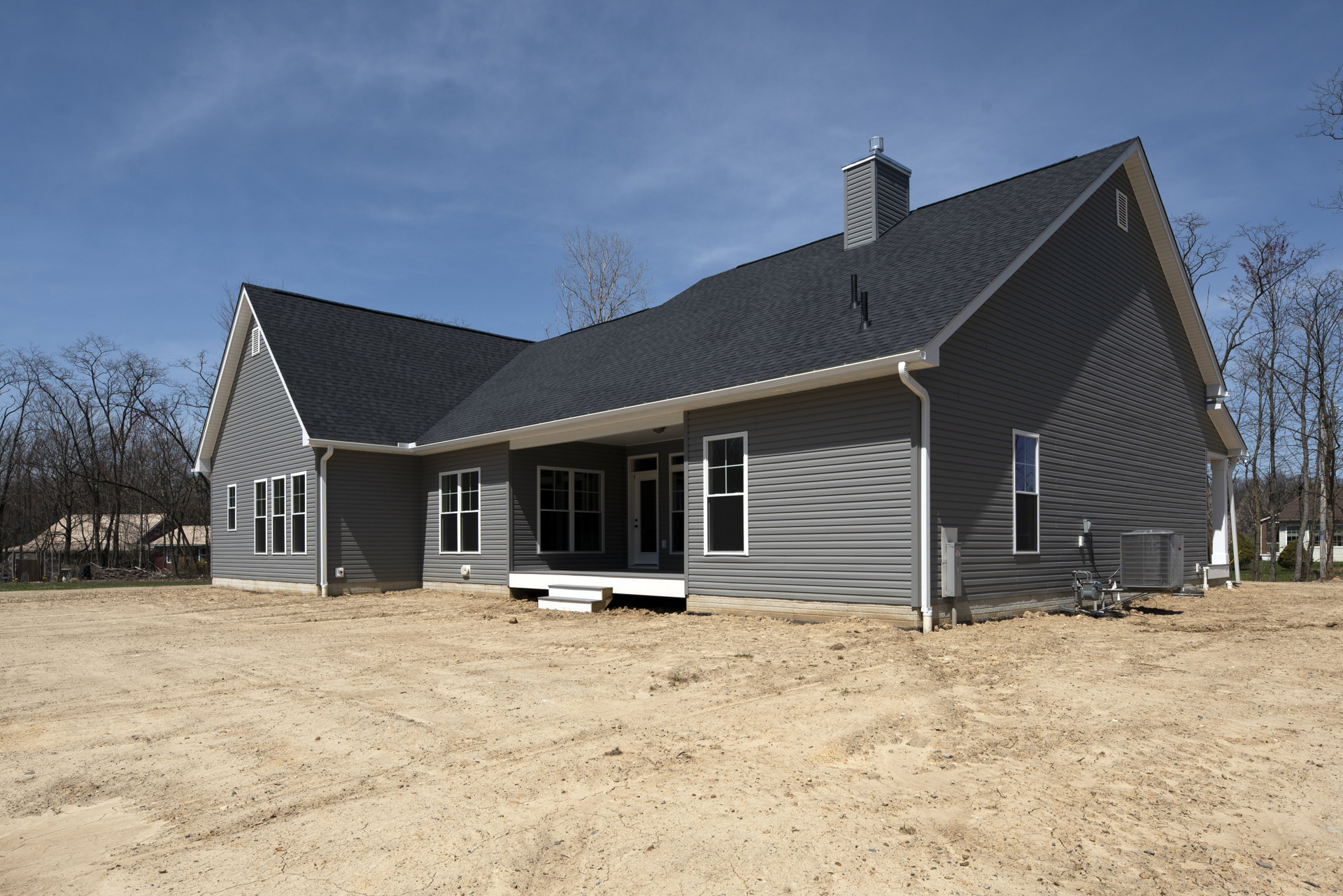 Two-story house with white-framed windows, brick chimney, and unfinished dirt yard under a partly cloudy sky