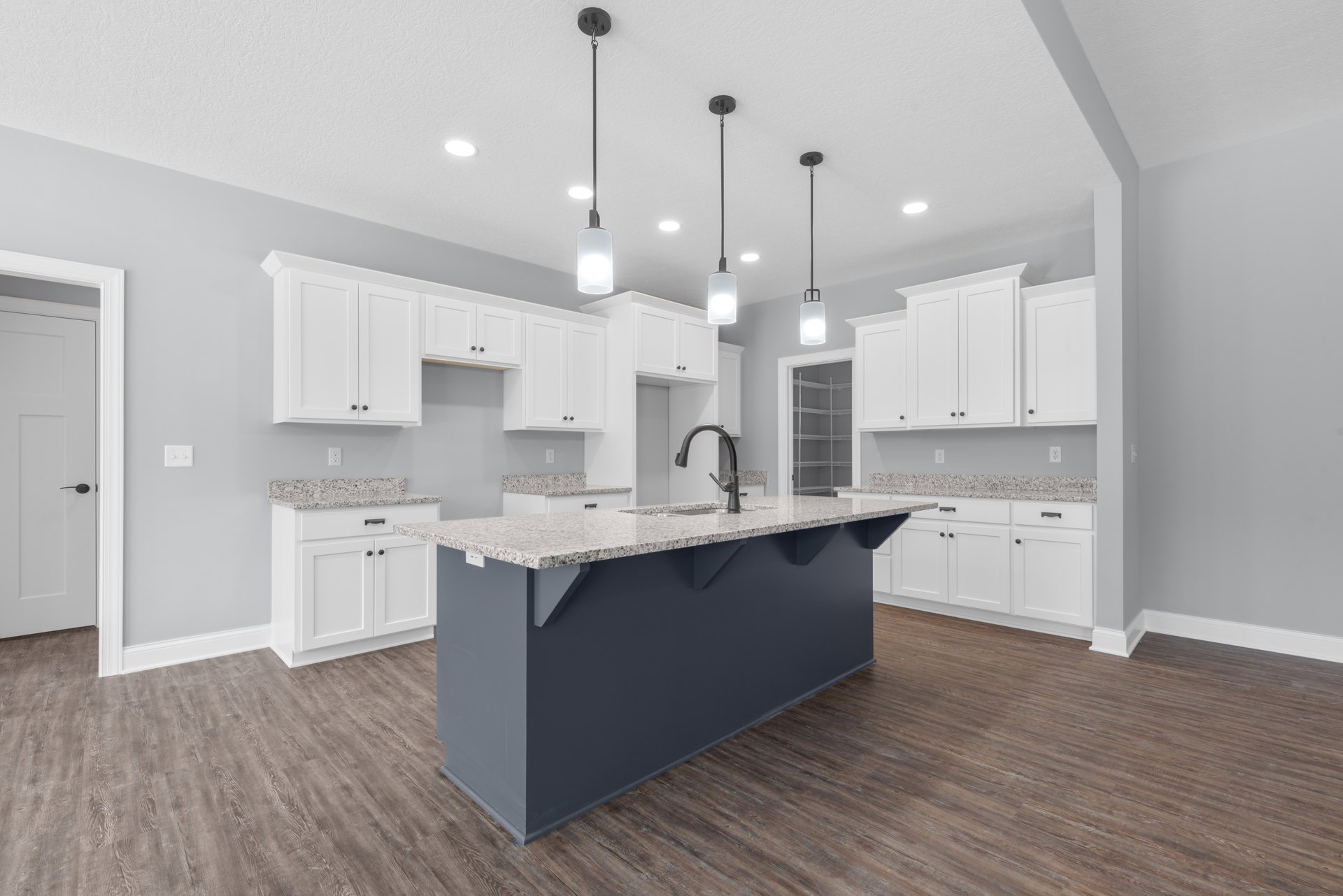 Kitchen featuring a central island with white cabinetry, light countertops, stainless steel sink, and black hardware; white door and built-in closet with shelving visible in