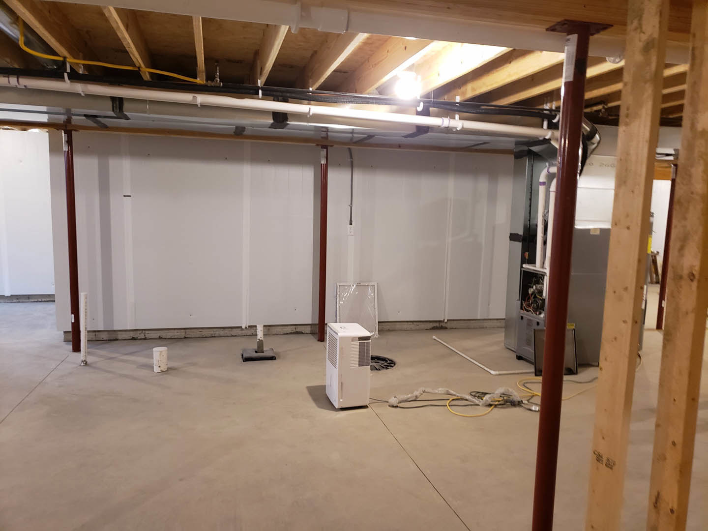 White-walled room with a white rectangular box featuring a vent, exposed ceiling beam, plastic-wrapped surface, visible wiring, and light fixture on the ceiling.