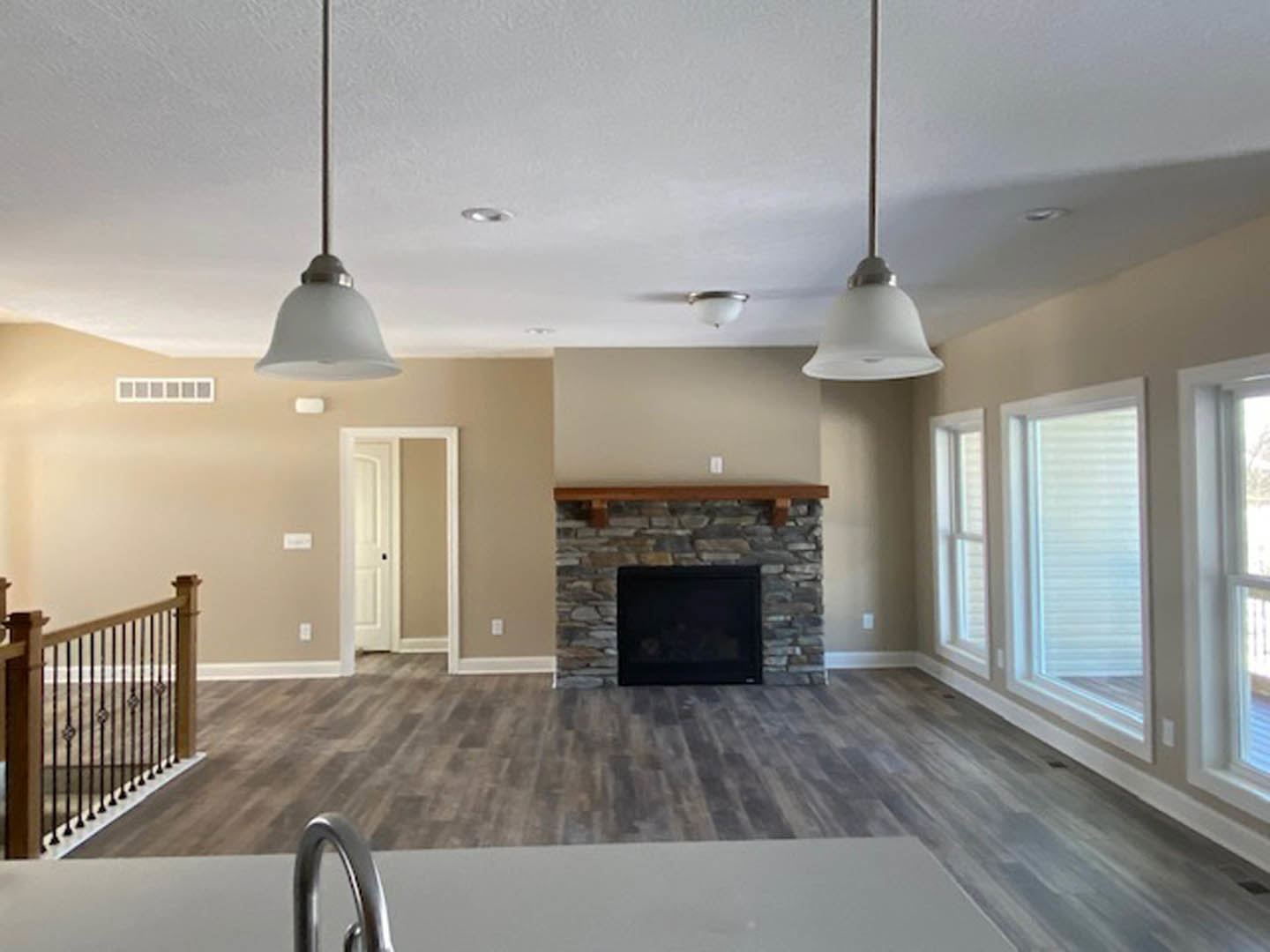 Living room featuring a brick fireplace with a wood mantel, wood flooring, black television mounted above the hearth, white door with black handle, and metal railing in foreground.