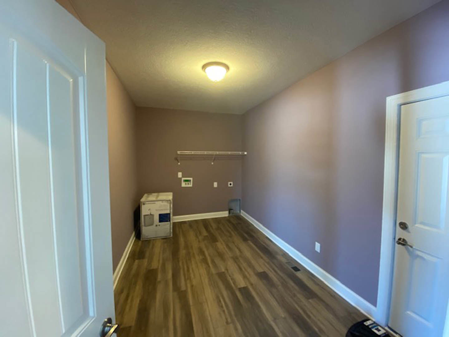 Hallway with light wood flooring, white walls, and a closed white door at the end