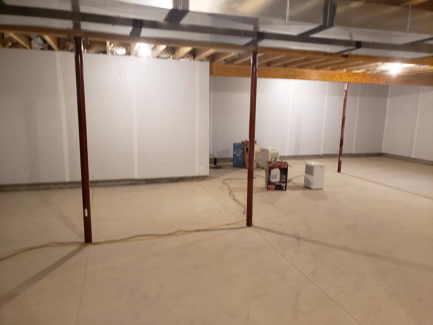 Empty room with white walls, concrete floor, exposed wooden beam, and metal object resting on the beam