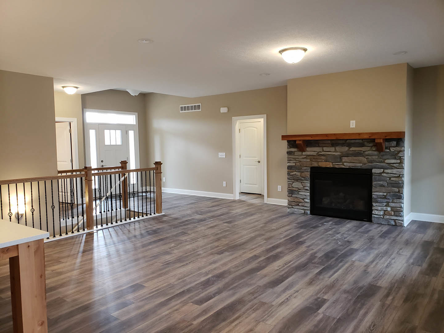 Living room with hardwood floor, stone fireplace featuring a wood beam mantel, white door with silver handle, and wood-grained ceiling beam