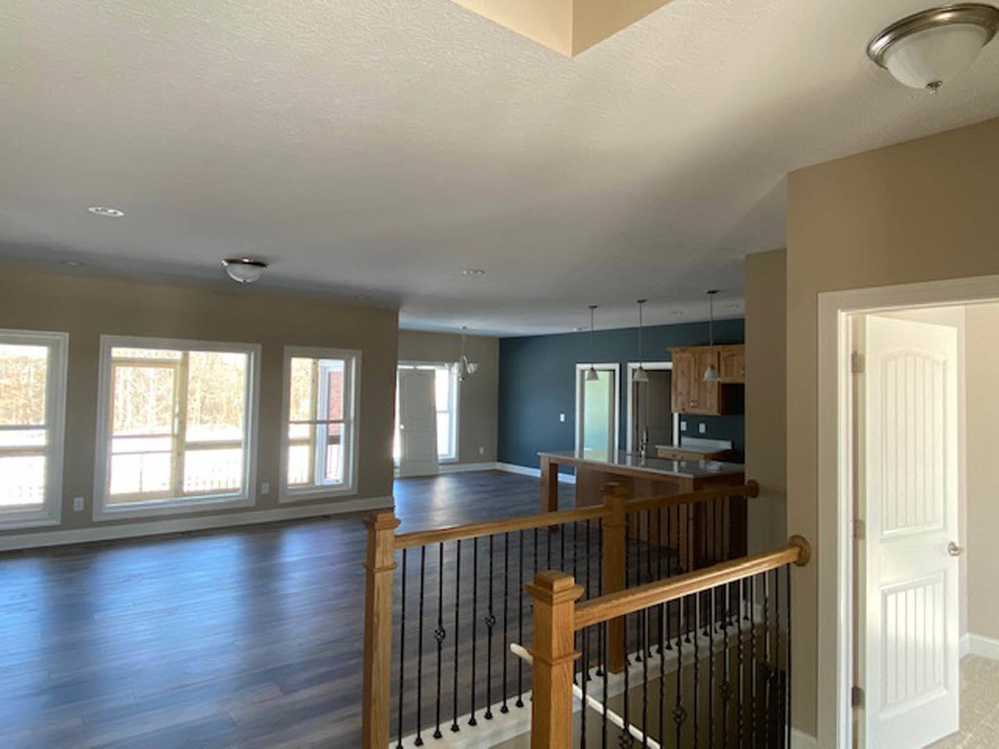 Open concept living area with light hardwood floors, wood staircase featuring black metal balusters, white framed window, white door, and modern ceiling light with white shade