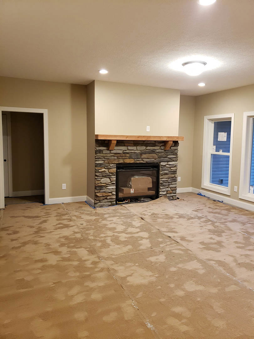 Living room with light carpet flooring, central fireplace featuring a box inside, white plaster walls, white door with a sign, and flat ceiling.