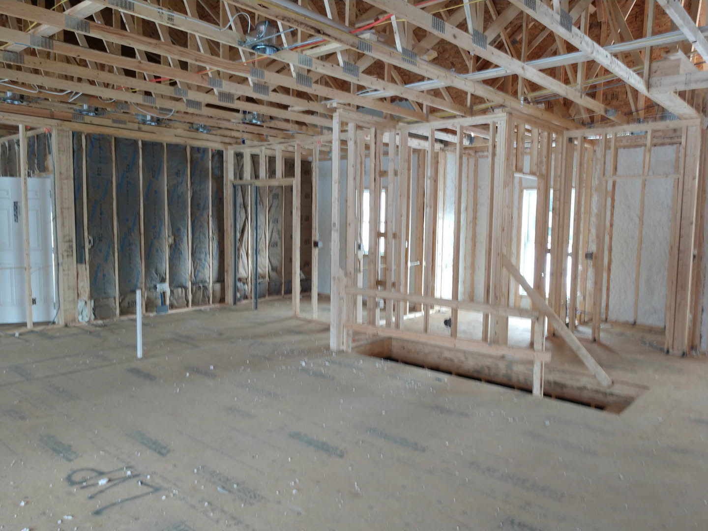 Living room with exposed wood ceiling beams, large window, white door, and unfinished wooden flooring