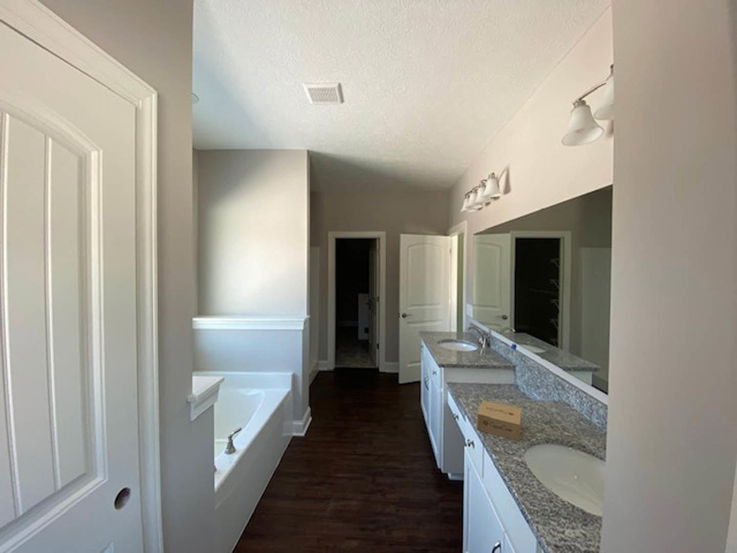 Bathroom with marble countertop, freestanding bathtub, dark wood flooring, white door with silver handle, white vent, and brown storage box on countertop.