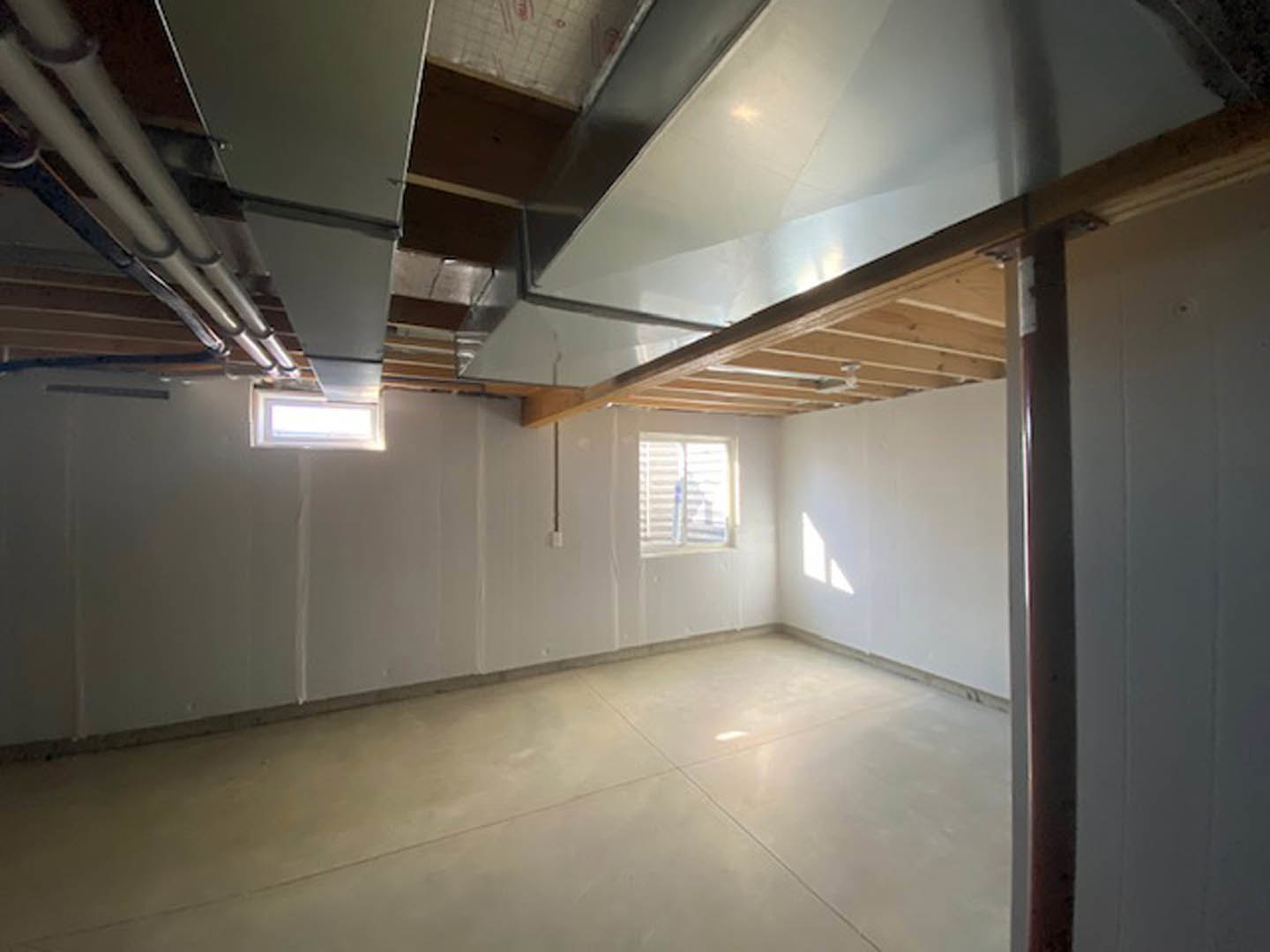 Living room with plaster ceiling, exposed beams, large window with blinds, tile flooring, fluorescent ceiling fixture, and visible pipes.