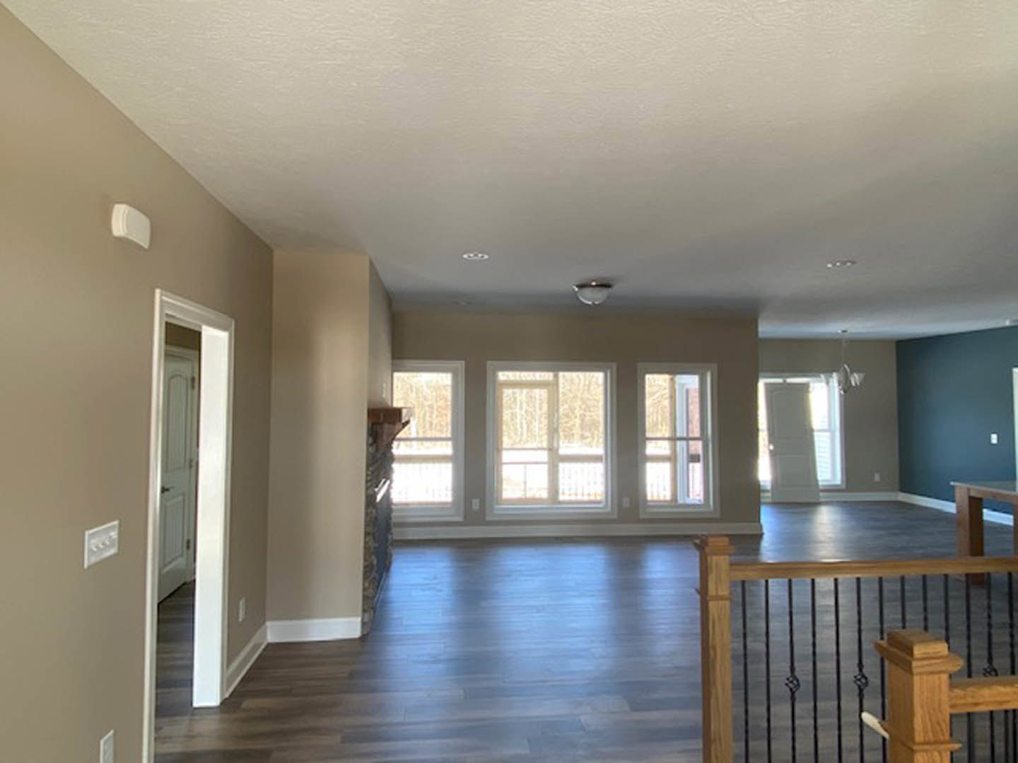 Open living area with wood flooring, staircase featuring wooden railing and black balusters, white walls with molding, window overlooking exterior, close-up of wall outlet and