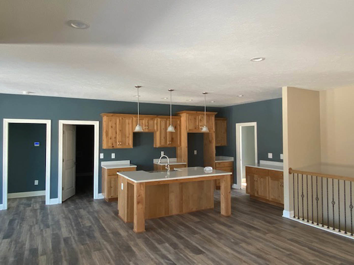 Open kitchen featuring natural wood cabinets, matching wood flooring, stone countertop with built-in sink, and a dining table; close-up details of railing and cabinetry visible.