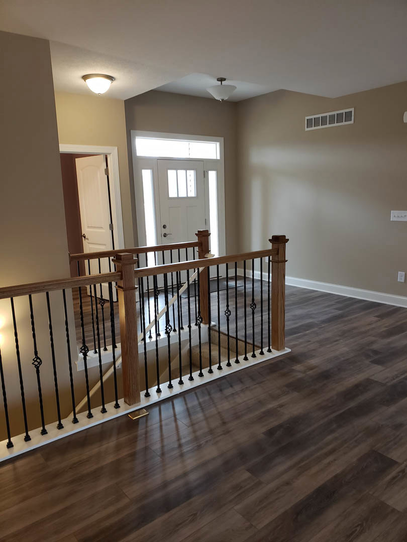 Wood staircase with matching wood flooring, white walls, wood handrail and balusters, ceiling light fixture, window with vent, and white door with glass panels.