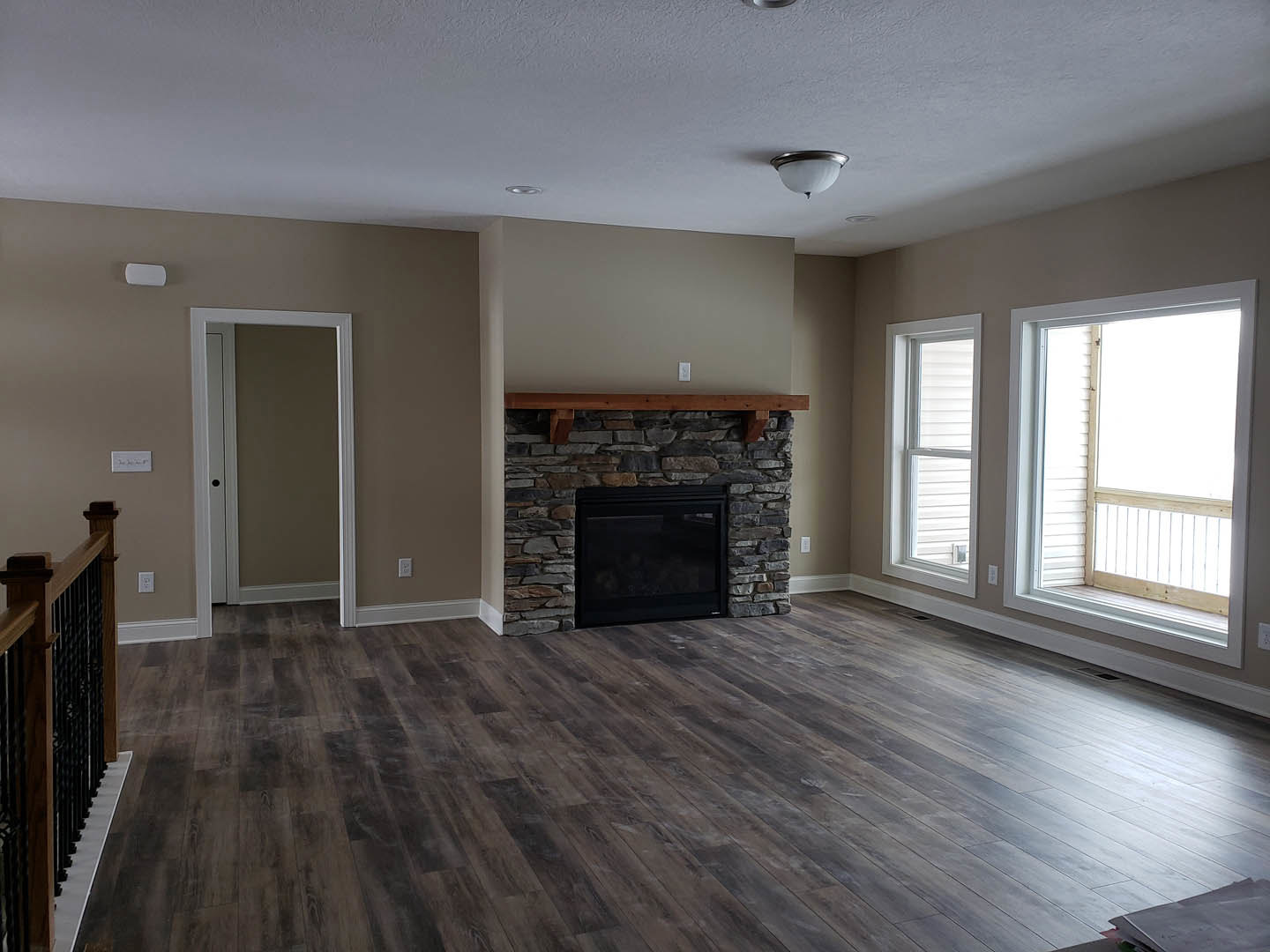 Living room with wide-plank hardwood floor, black fireplace set in a stone accent wall, wood beam mantel, white-trimmed door and window