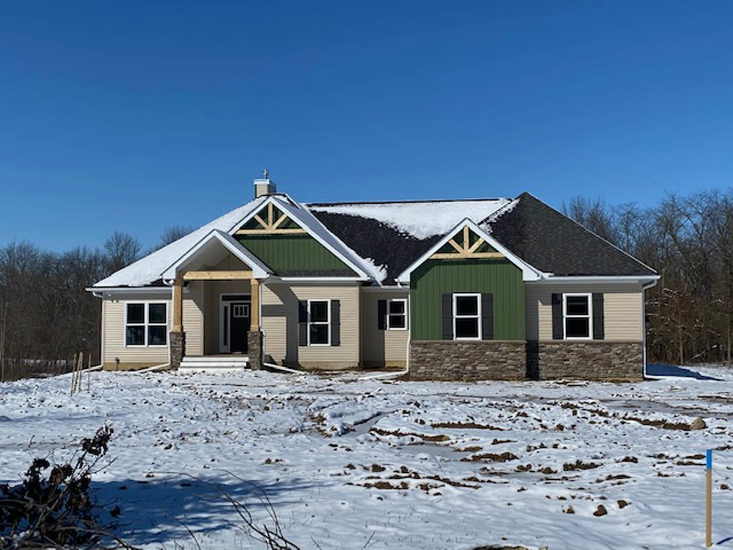 Two-story house with snow-covered roof and ground, stone accent wall, black-framed windows, and covered front porch