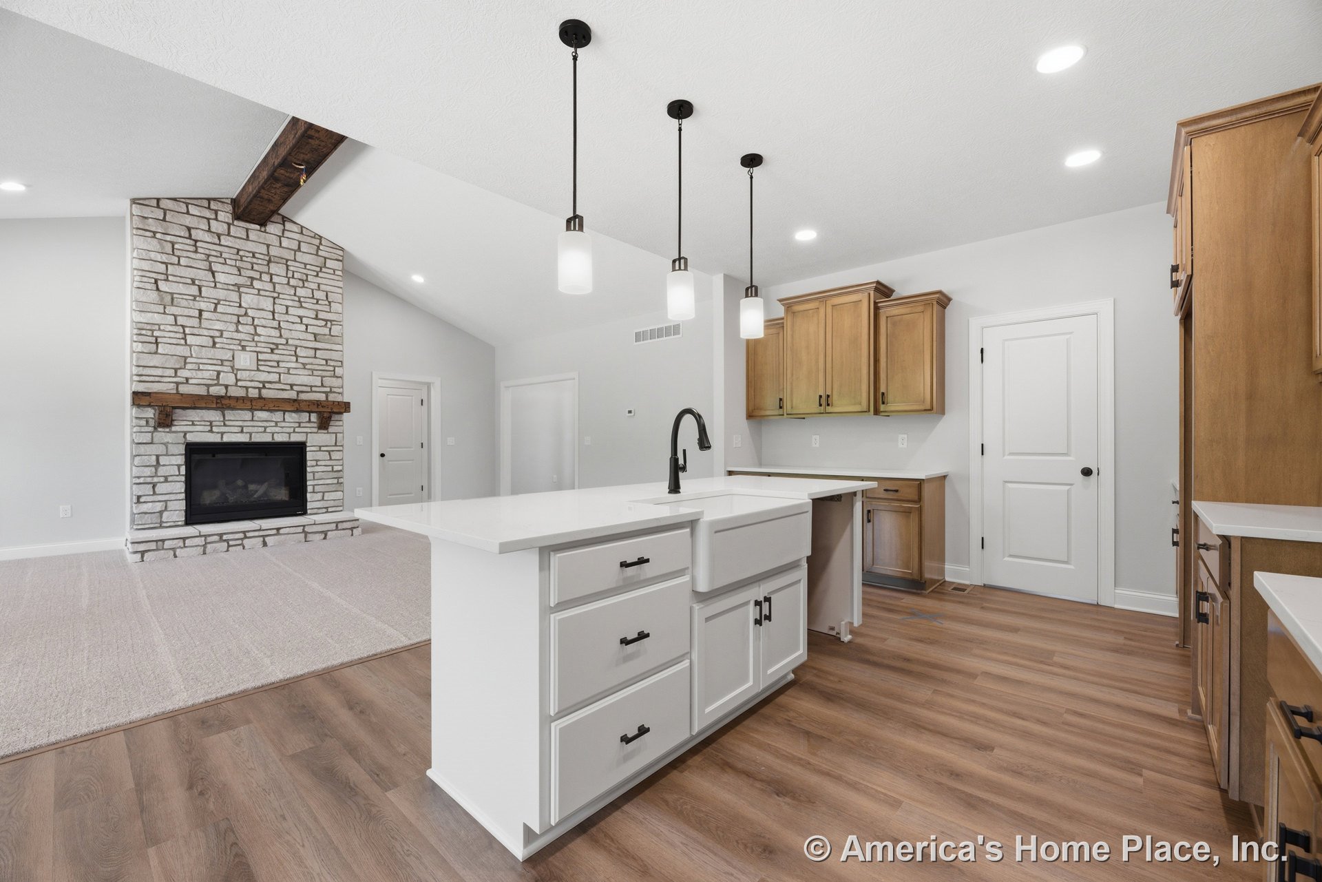 Open kitchen with white shaker cabinets, quartz countertops, large island with farmhouse sink, vaulted ceiling featuring exposed wood beam, pendant and recessed lighting; adjacent