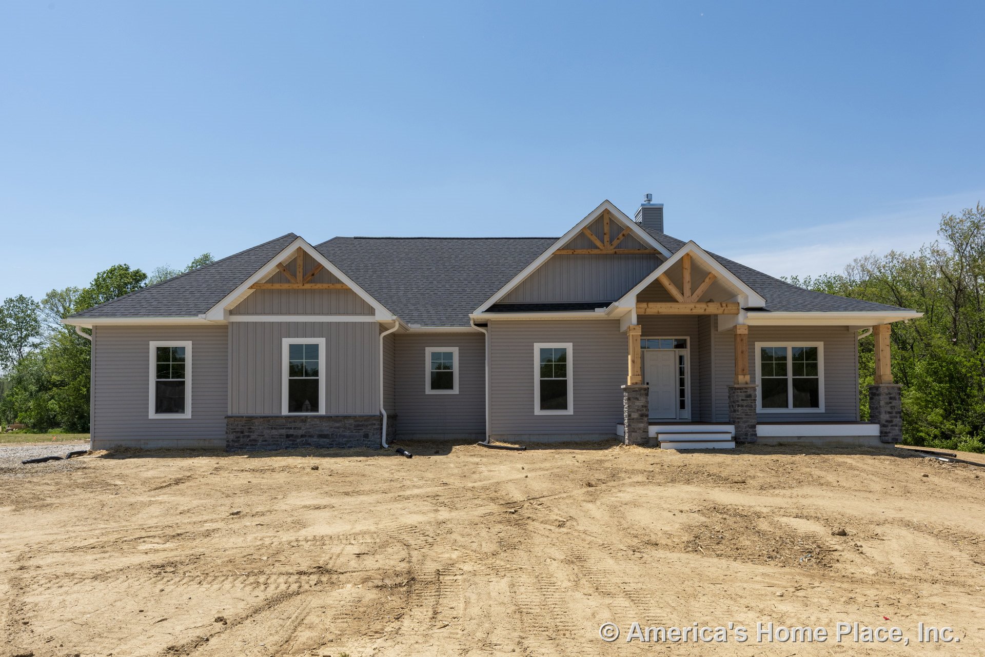 Covered front porch with exposed wood trusses and stone columns, gray vinyl siding, stone veneer foundation, white trim windows, gabled roof with architectural shingles, new