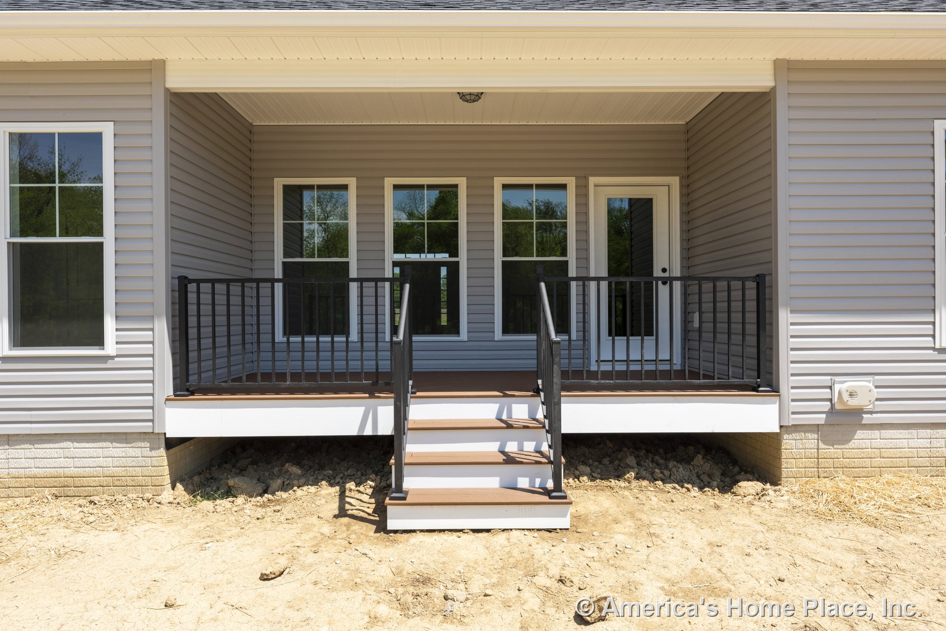 Covered back porch with composite deck flooring, black metal railings, three large windows, glass-paneled exterior door, vinyl siding exterior, white trim, steps leading to yard