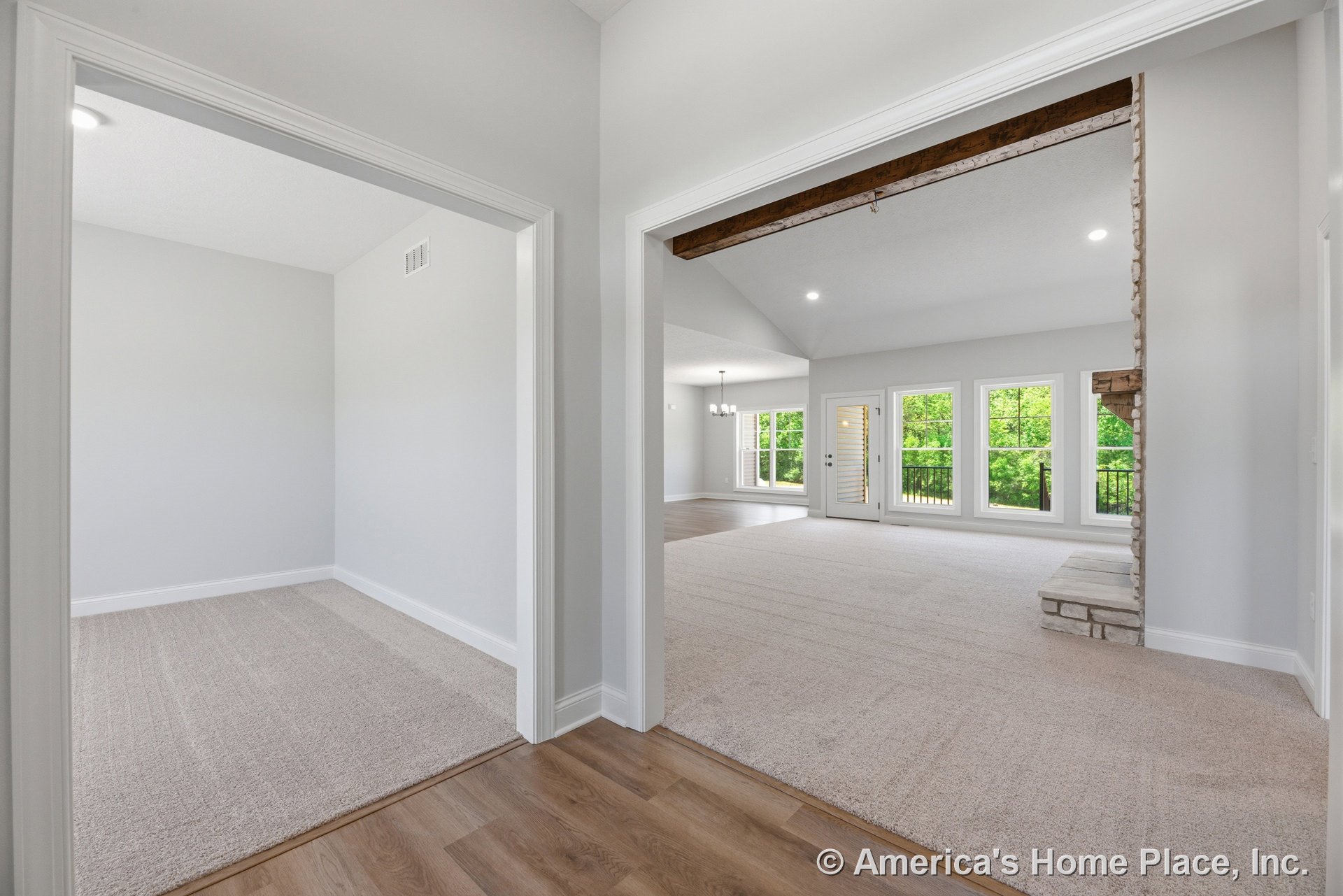 Vaulted ceiling with recessed lighting, stone fireplace with wood mantel, expansive windows overlooking greenery, carpeted living area, wood-look flooring in entryway, white trim