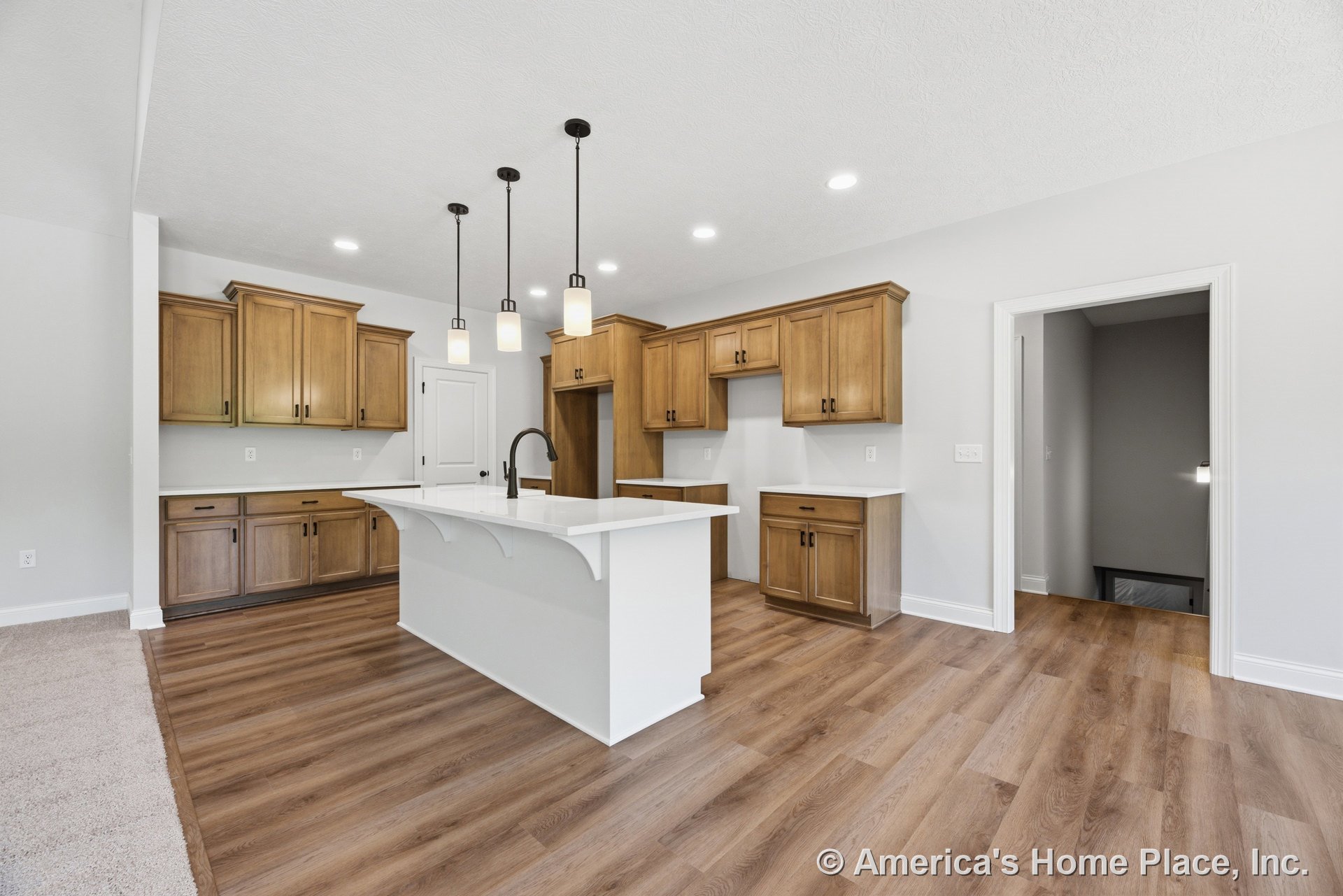 Wood upper and lower cabinets with white quartz countertops, large central kitchen island topped with quartz, three modern pendant lights above the island, vinyl plank flooring