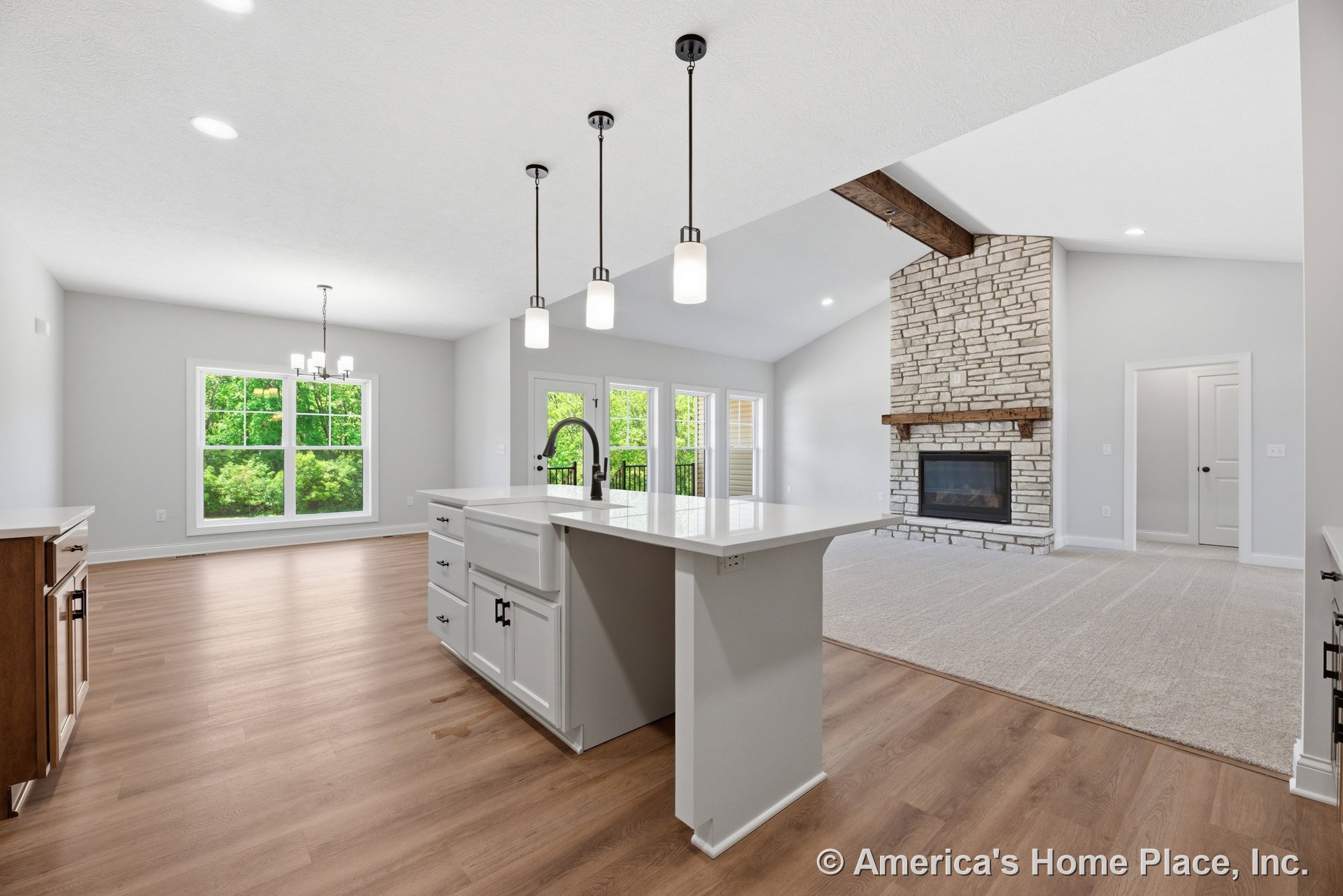 Open kitchen and living area with vaulted ceiling, stone fireplace and wood mantel, white cabinetry and kitchen island with farmhouse sink, quartz countertops, wood-look flooring