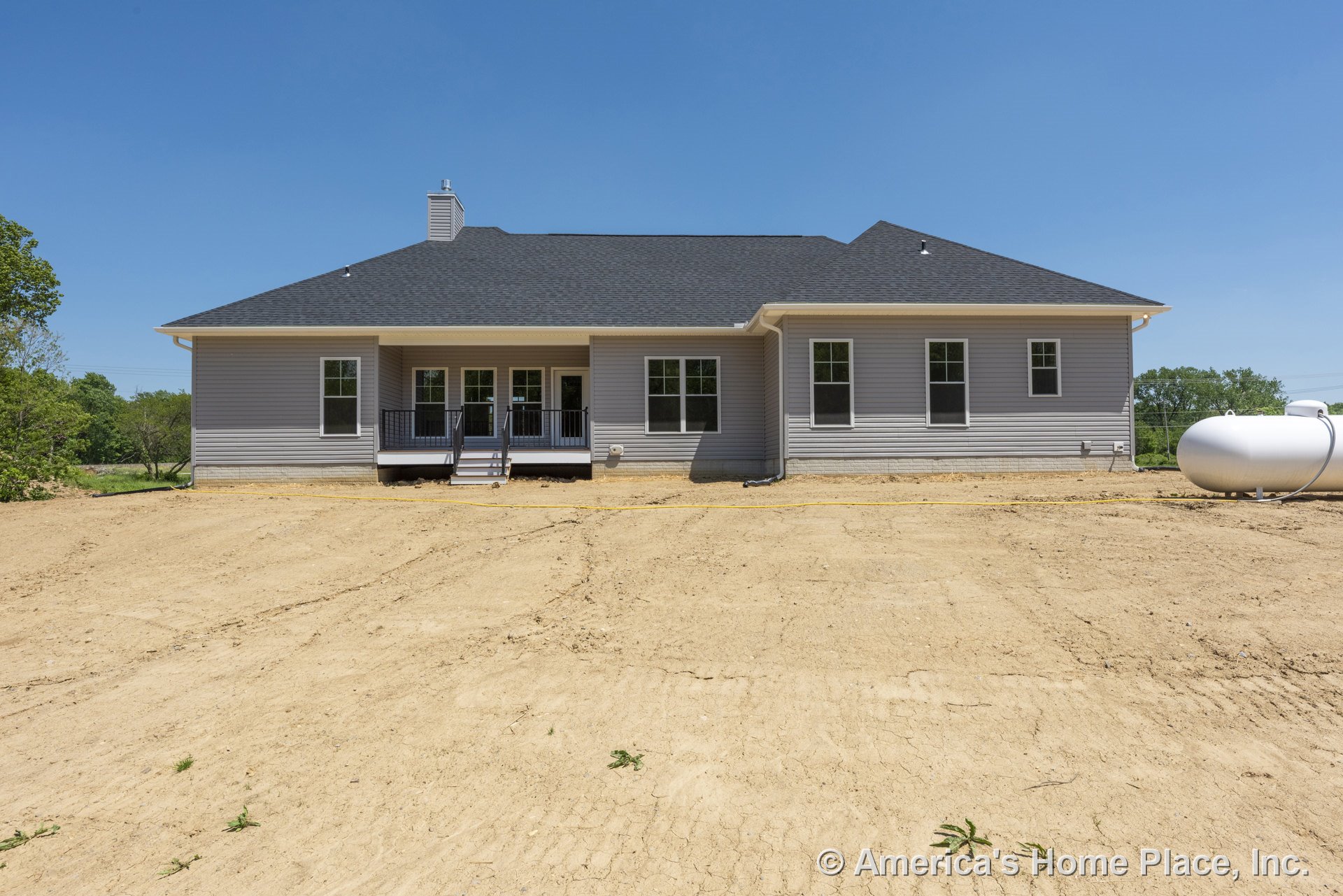 Gray vinyl siding exterior with covered back porch featuring black railings, multiple double-hung windows, asphalt shingle roof, white trim, back entrance steps, and visible
