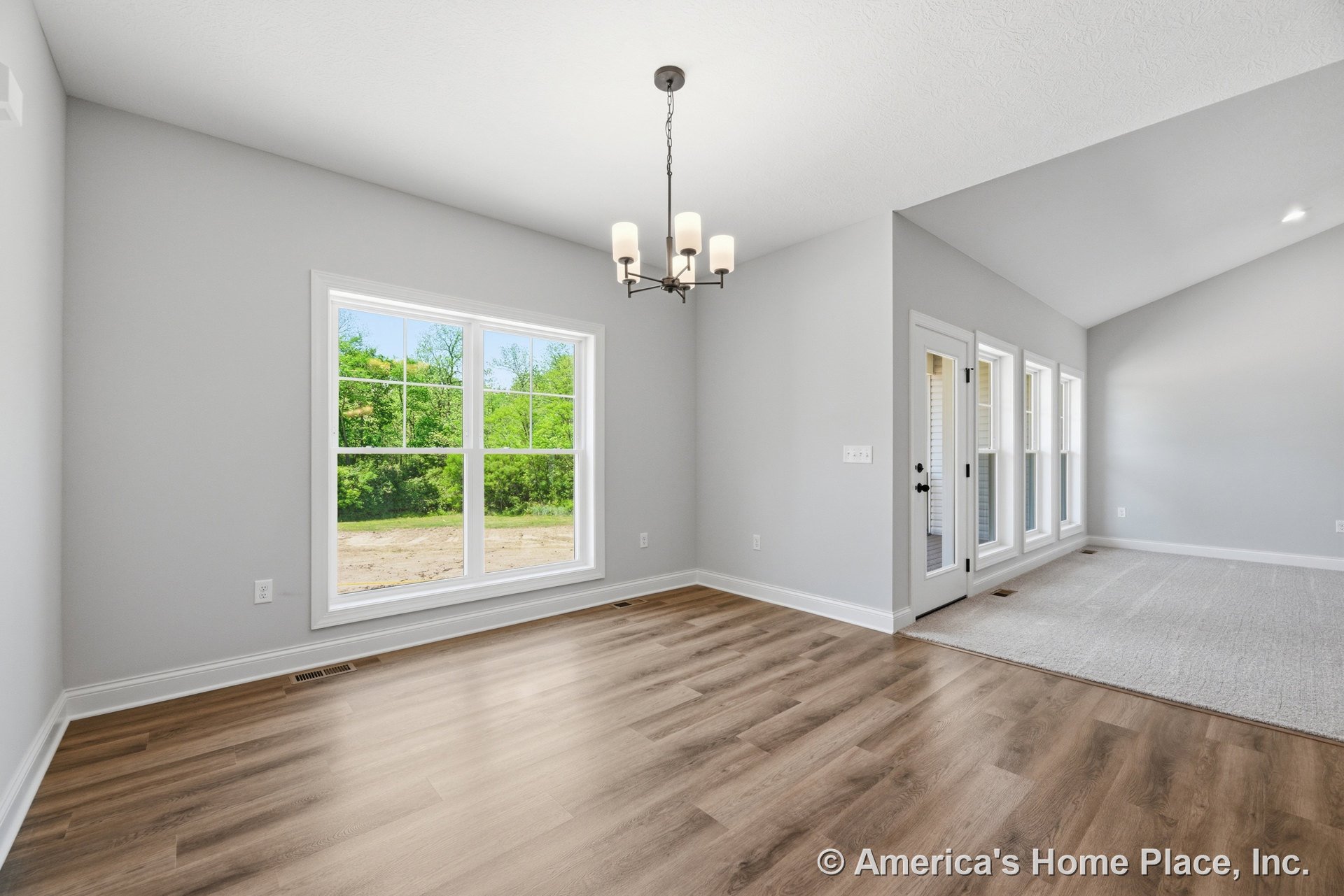 Dining area with light wood-look flooring, large double-hung windows, modern chandelier, vaulted ceiling, and seamless transition to carpeted living room featuring French doors