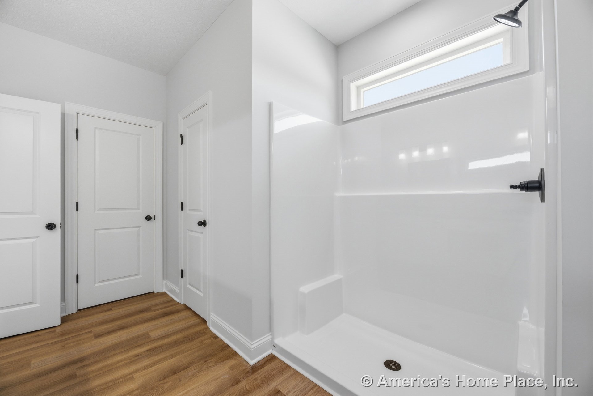 Walk-in shower with built-in bench, matte black shower fixture, horizontal transom window, white paneled doors, and wood-look flooring.