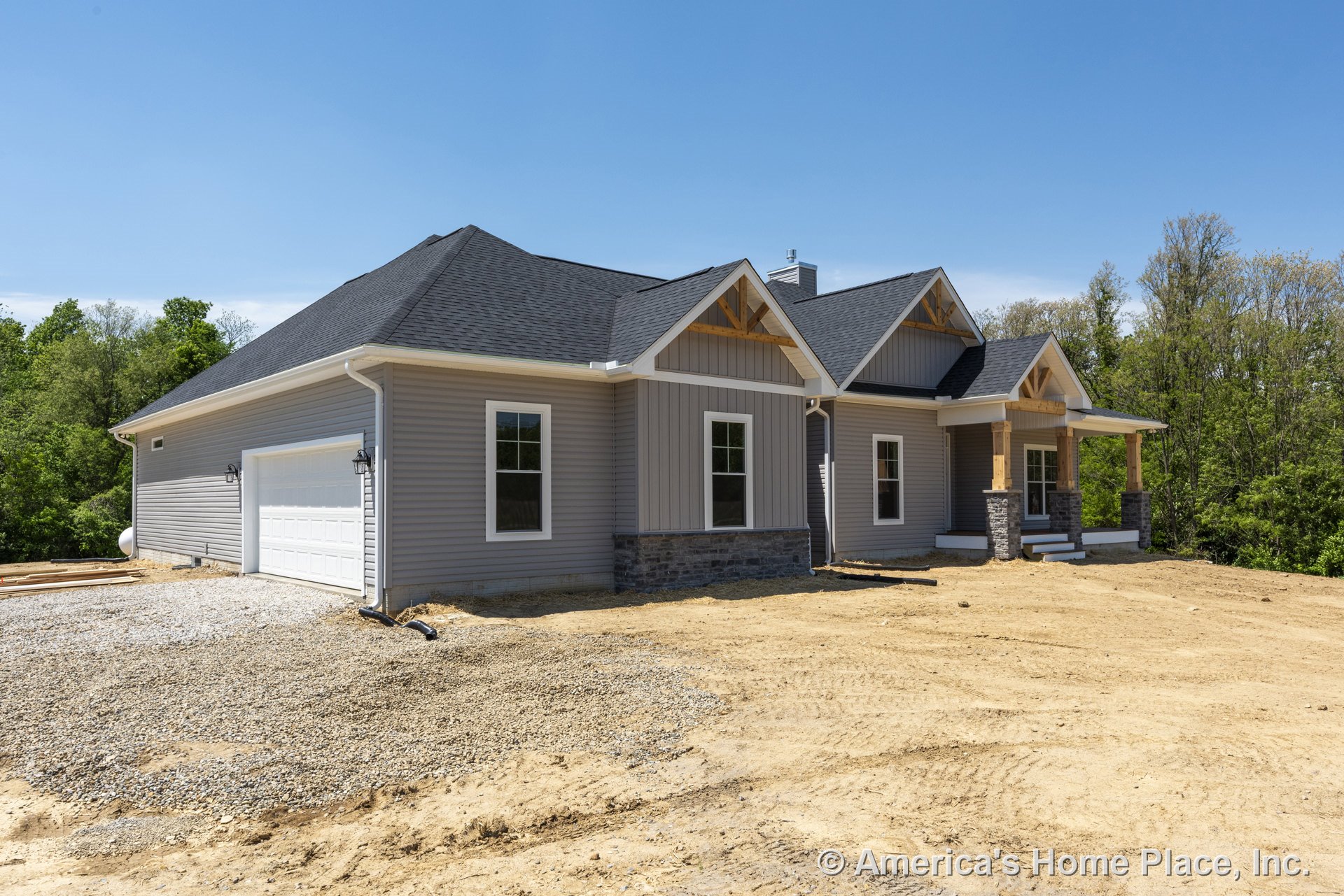 Gray vinyl siding with vertical and horizontal panels, stone accents, white framed windows, attached two-car garage, gable roof featuring exposed trusses, covered front porch with