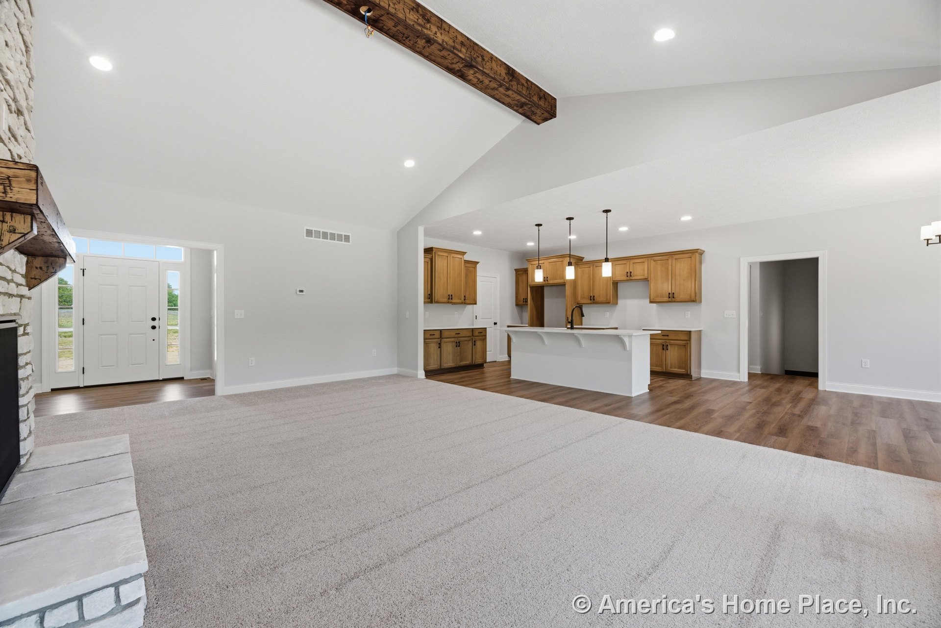Vaulted ceiling with exposed wood beam, stone fireplace with wood mantel, open kitchen featuring wood cabinetry, white quartz island, recessed and pendant lighting, carpet and wood