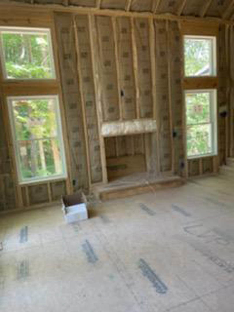 Living room with wood plank walls, hardwood flooring, large windows, and a fireplace; bookshelf and white object visible in background.