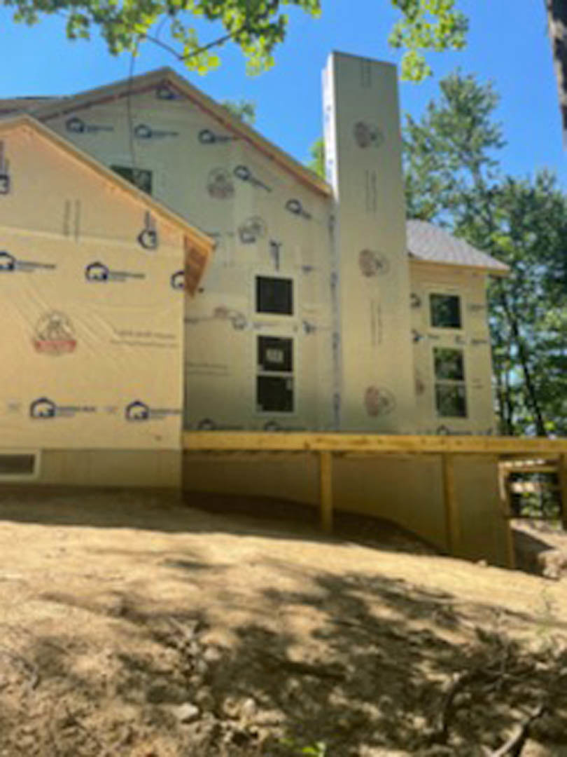 Two-story house with gray siding, white trim, prominent brick chimney, large windows, and mature trees in the yard