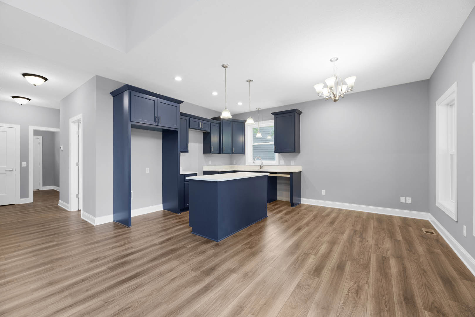 Blue kitchen cabinets with brushed metal hardware, white quartz countertops, hardwood flooring, stainless steel sink, and a modern chandelier hanging from a plaster ceiling.