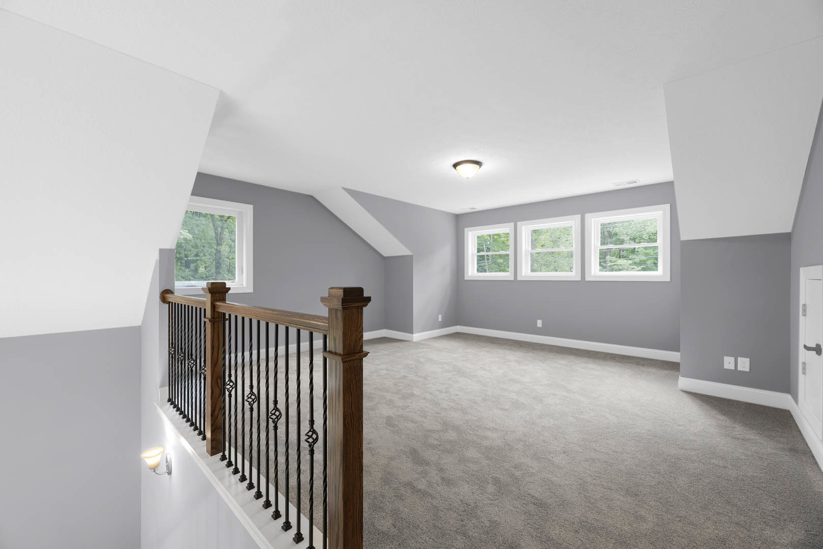 Carpeted upstairs landing with white railing, multiple windows overlooking trees, recessed ceiling light, neutral walls