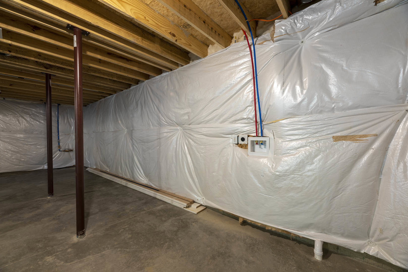 White plastic wall covering with exposed wooden beam, white pipes, a white box featuring a window and colorful valves, and red and blue pencils resting on a white surface.