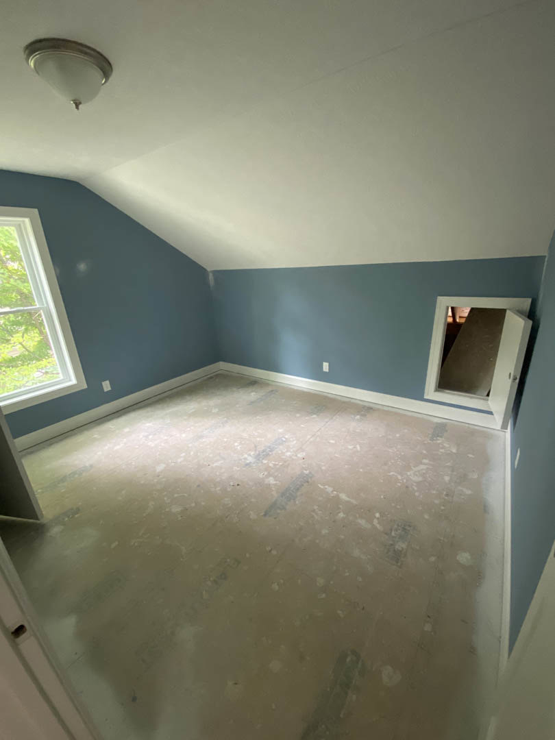 Blue accent wall with small white-framed window, white surrounding walls, ceiling light fixture, and plaster finishes in a residential interior.