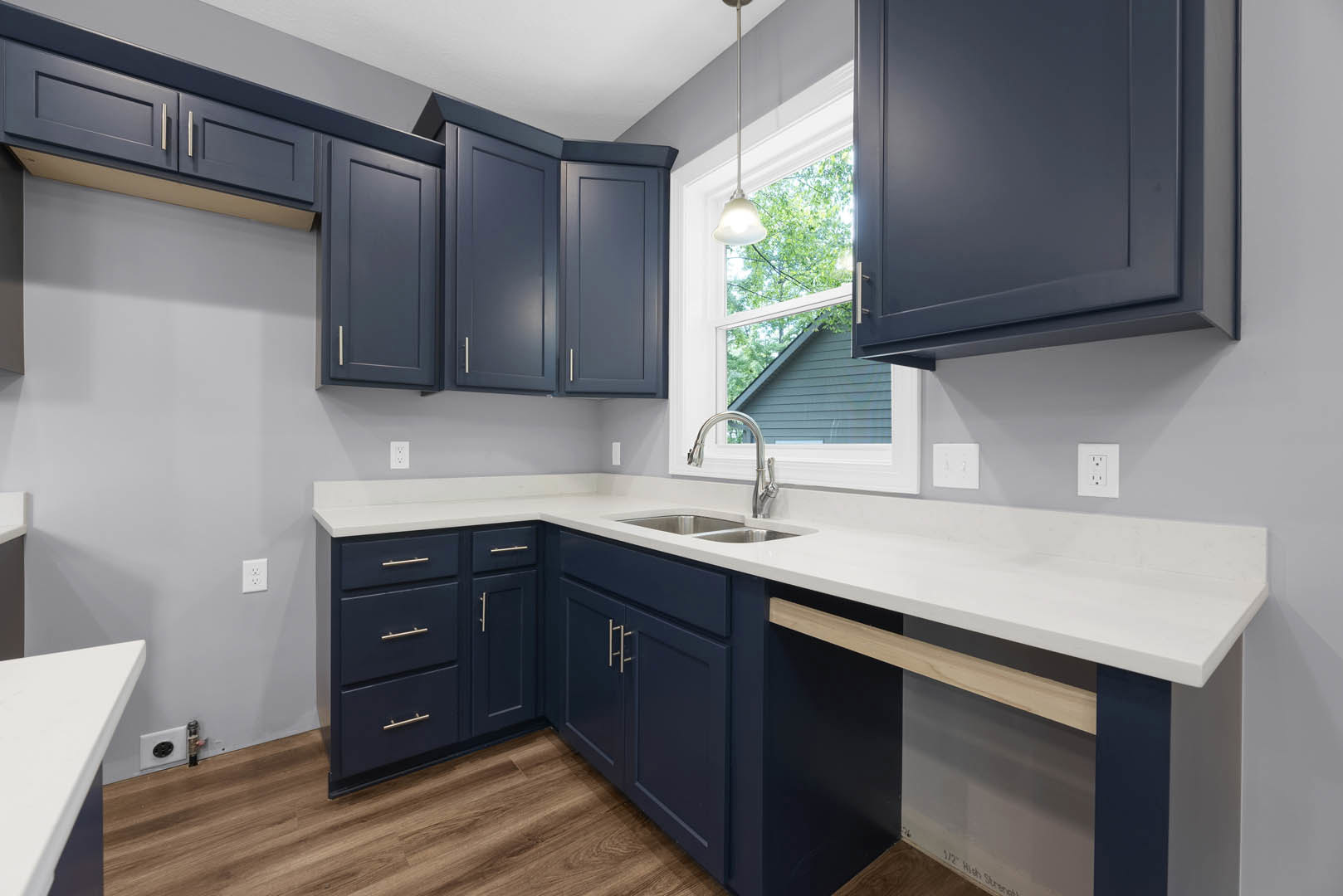 Dark blue kitchen cabinets with brushed metal handles, white quartz countertop, stainless steel sink, white backsplash, and a white electrical outlet on the wall.